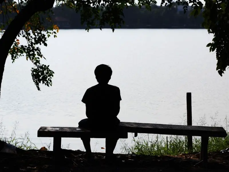 Lonely man sitting by a lake, lost in thought