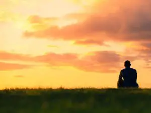 Man sitting on grass, looking at a fiery sky