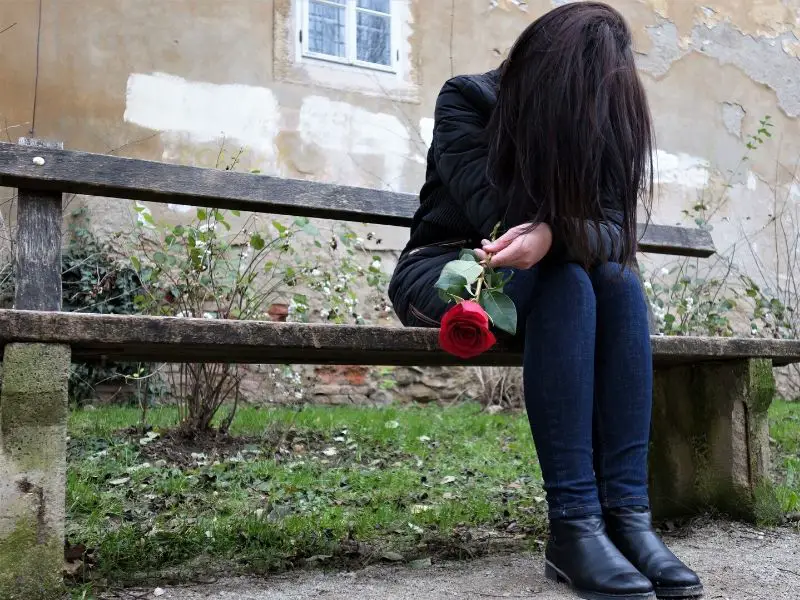 Grieving woman sitting on a bench with a rose in her hand