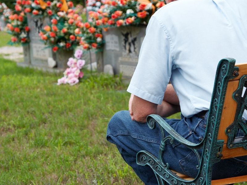 Man sitting on a bench by the grave 