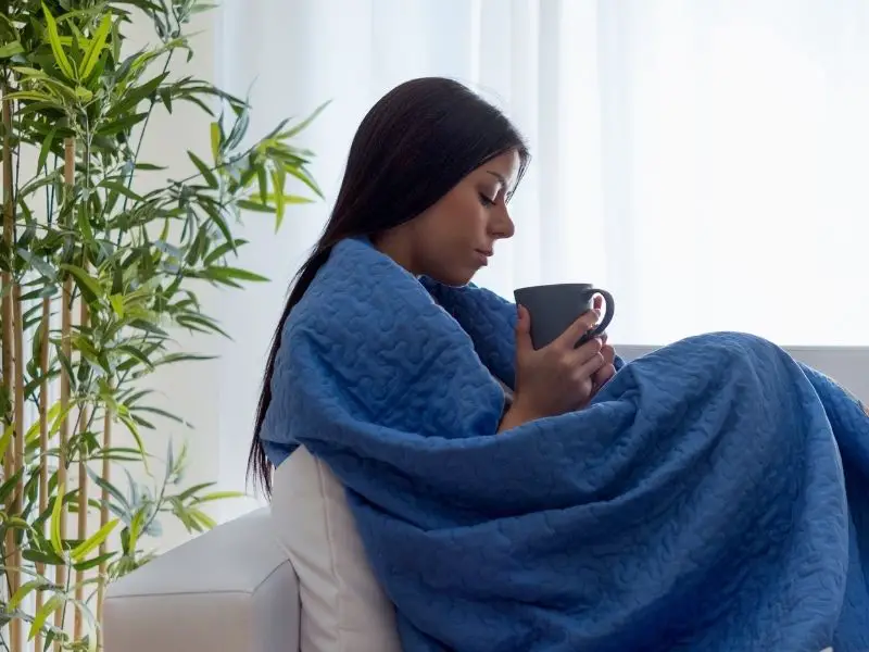 Sad woman drinking tea while wrapped in a blanket